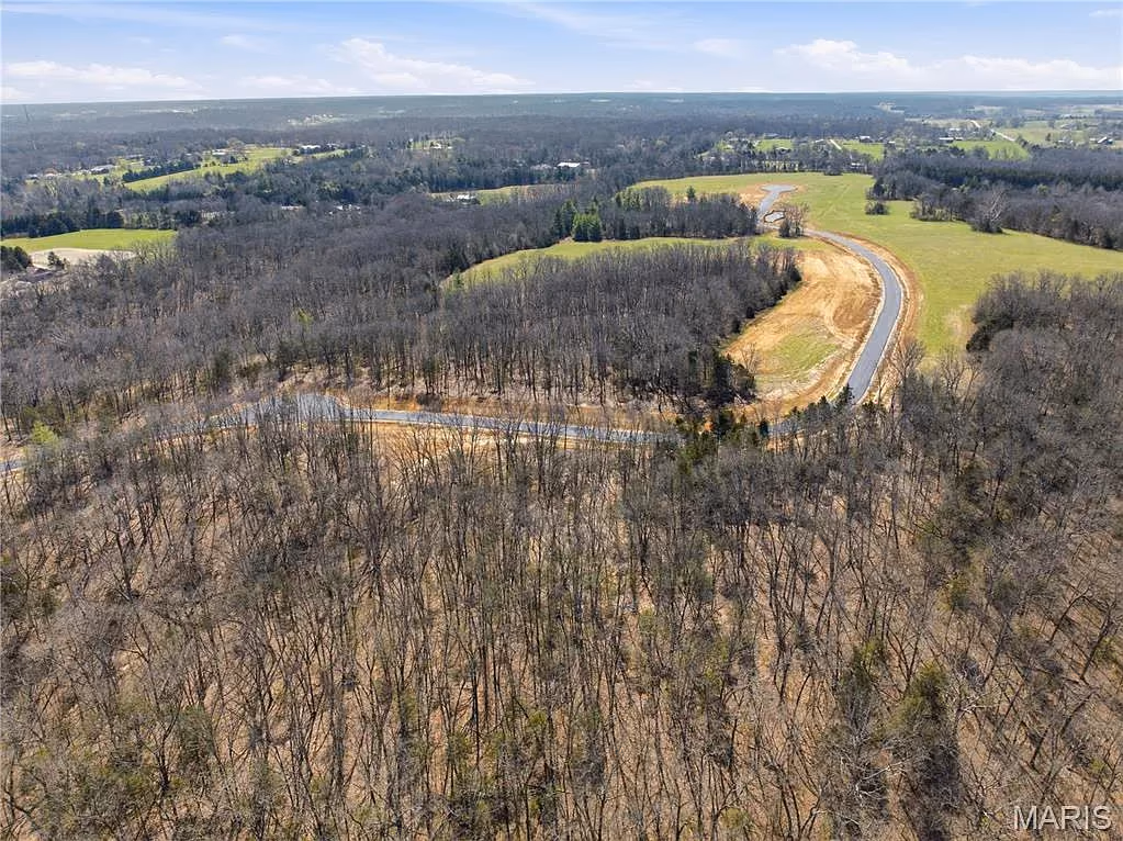 Road sweeping around a wooded ridge toward open fields