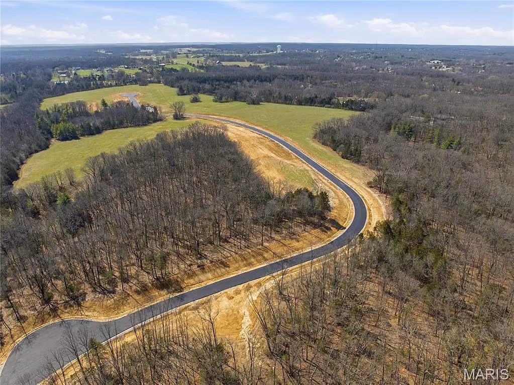 Road bending around a wooded knoll beside open meadow